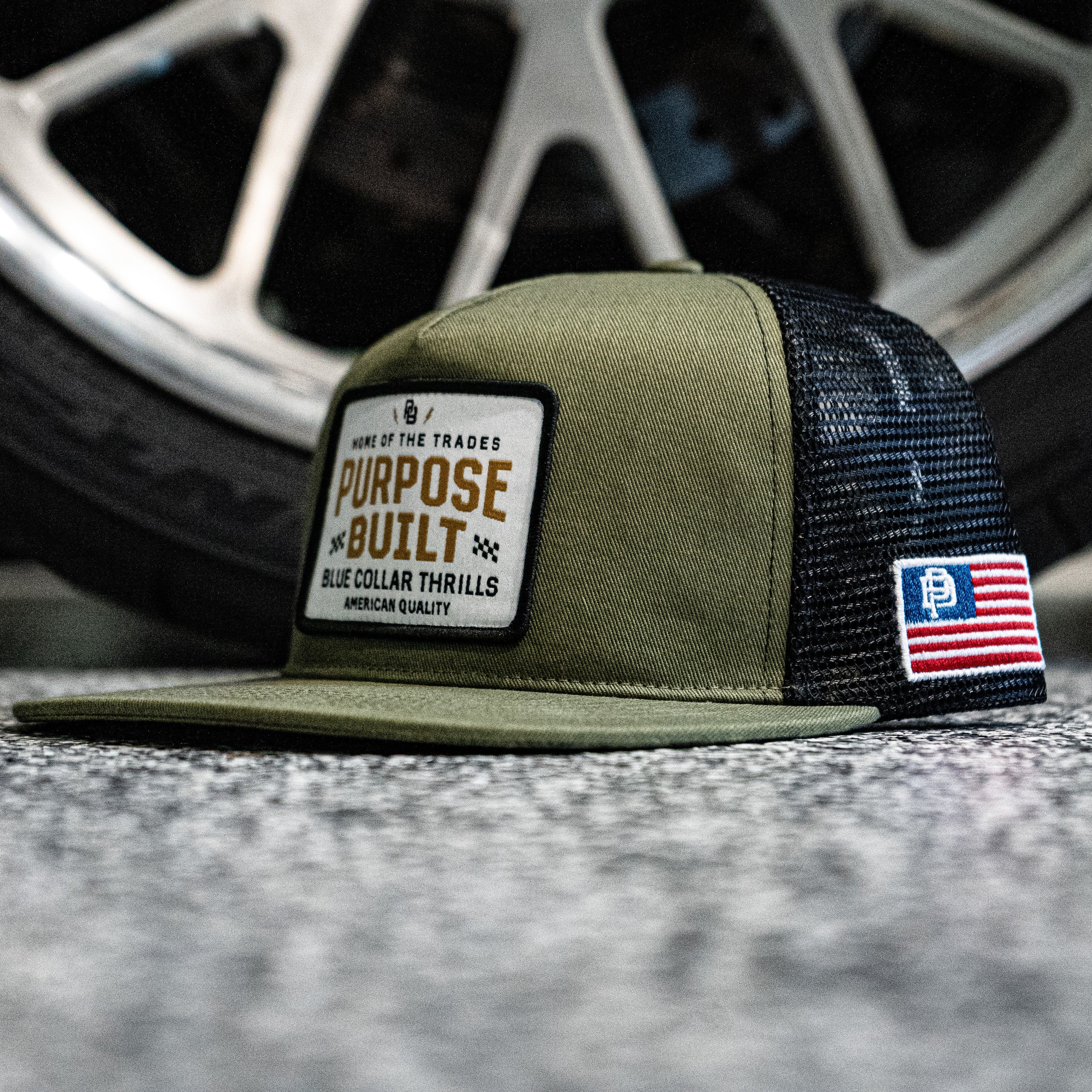 Green and black cap with branding on a textured surface with a blurred wheel in the background