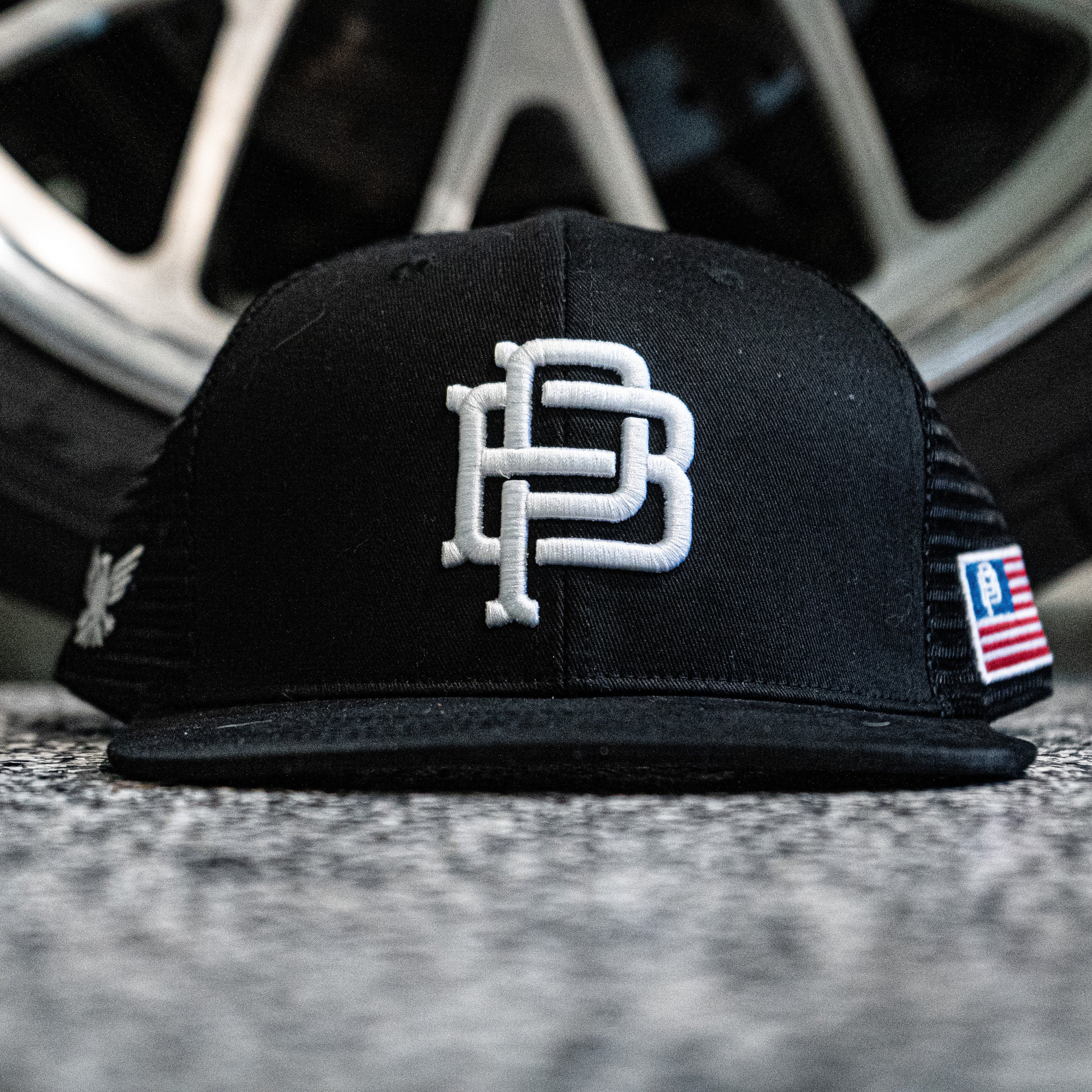 Black cap with a logo on a textured surface with a blurred wheel in the background